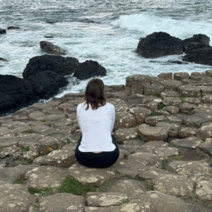a woman sitting on a rock overlooking the ocean at wholehearted living institute